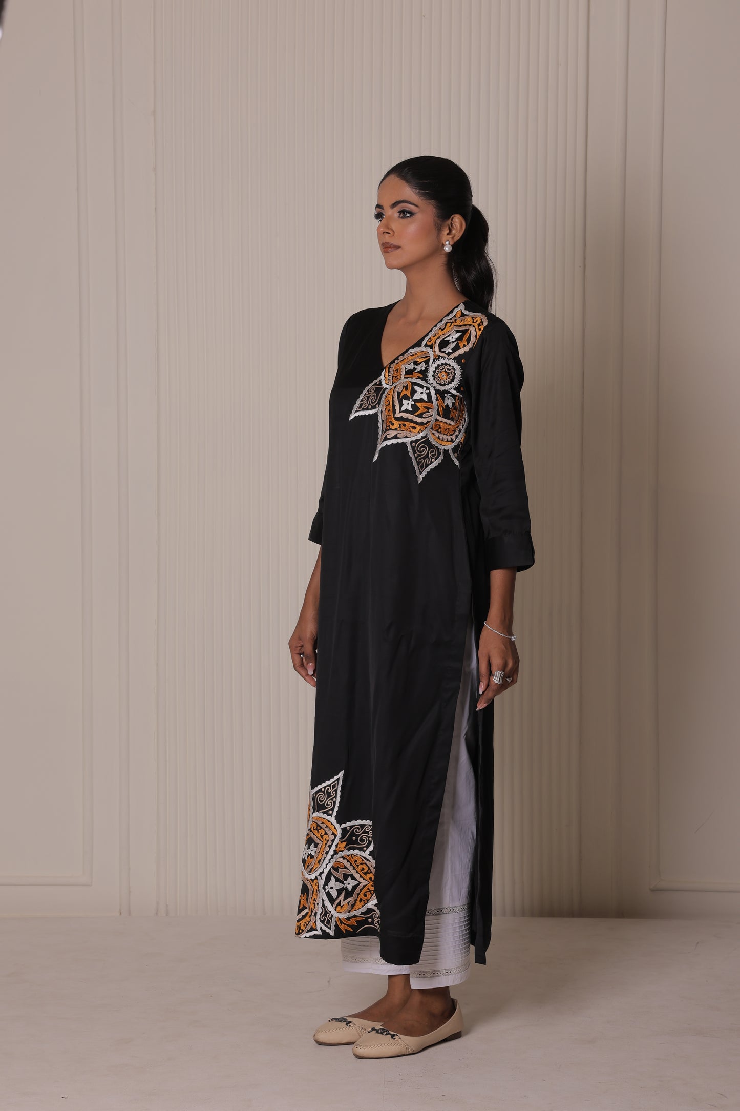 Woman wearing a black outfit with intricate embroidery against a plain background